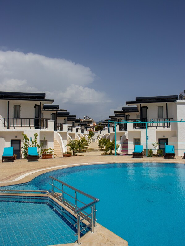 A pool area with a clear blue pool, lounge chairs, and a building with white walls and balconies.