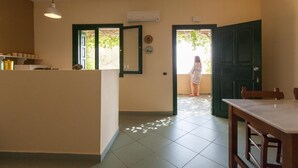 Habitació amb zona de cuina, taula de menjador i vista cap a un espai exterior per una porta oberta.