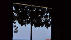 Habitació amb gran finestra que domina una vista costanera, incloent un edifici blanc amb cúpula vermella i vegetació.