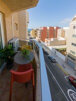 Ein Balkon mit Tisch und Stühlen, mit Blick auf eine Straße mit parkenden Autos und Gebäuden.