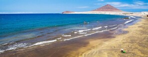 Una playa con agua azul cristalina, una orilla arenosa y una montaña al fondo.