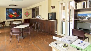 A hotel room with a dining area, a kitchen counter, a bookshelf, and a large painting on the wall.