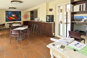 Una camera d'albergo con zona pranzo, angolo cottura, libreria e un grande quadro appeso al muro.