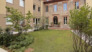 A courtyard with a lawn, trees, and a building with multiple windows and a door.