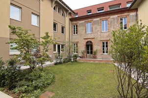 Un cortile con prato, alberi e un edificio con diverse finestre e un ingresso.