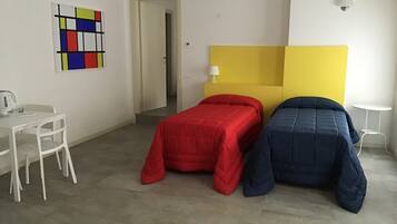 Habitación de hotel con dos camas, un escritorio con silla, una mesita y una obra de arte colorida en la pared.