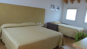 A room with two beds, a small table, and two windows.
