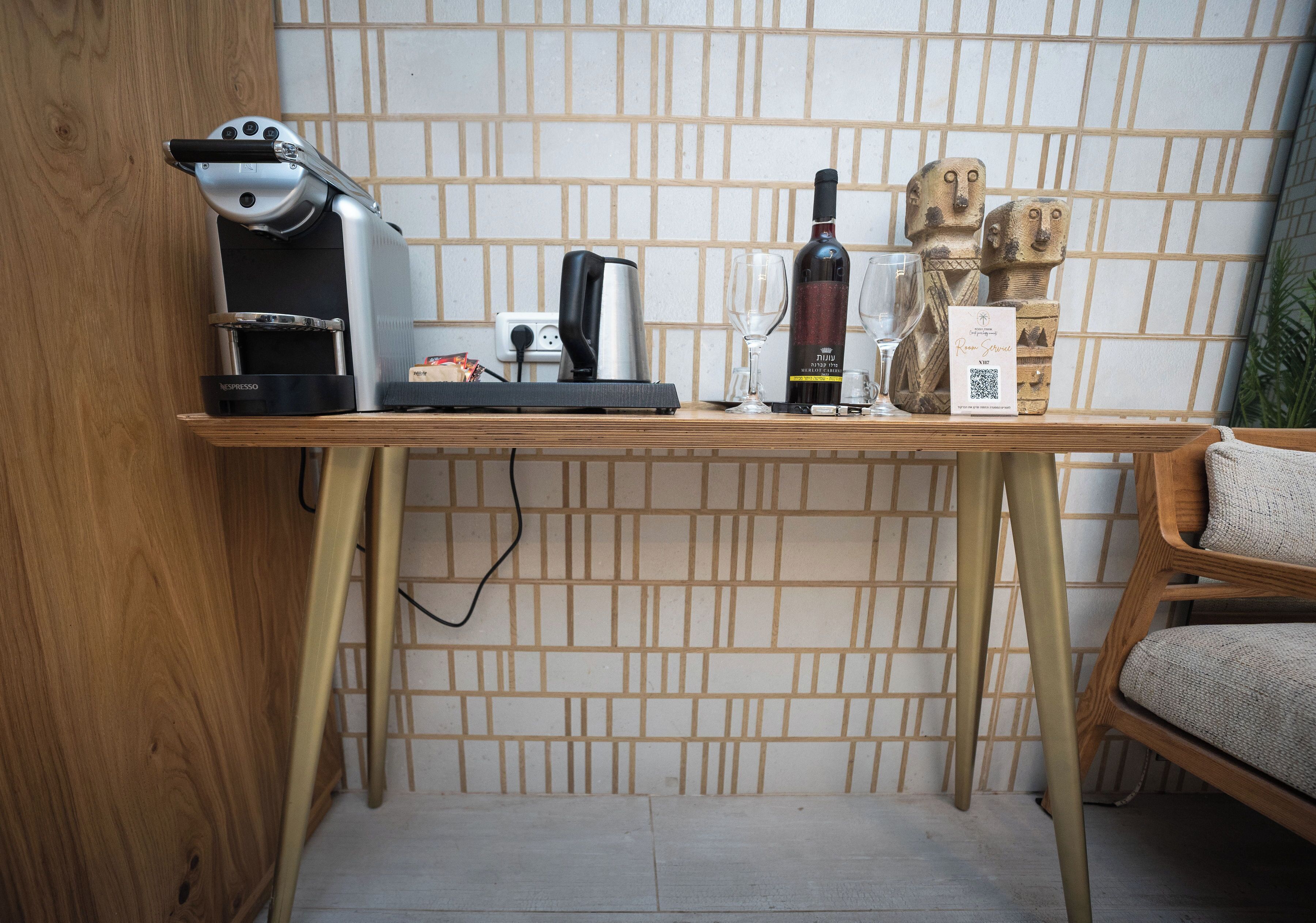 Un petit coin cuisine comprenant une machine à café, une bouteille de vin et des objets décoratifs, le tout posé sur une table en bois devant un mur carrelé.