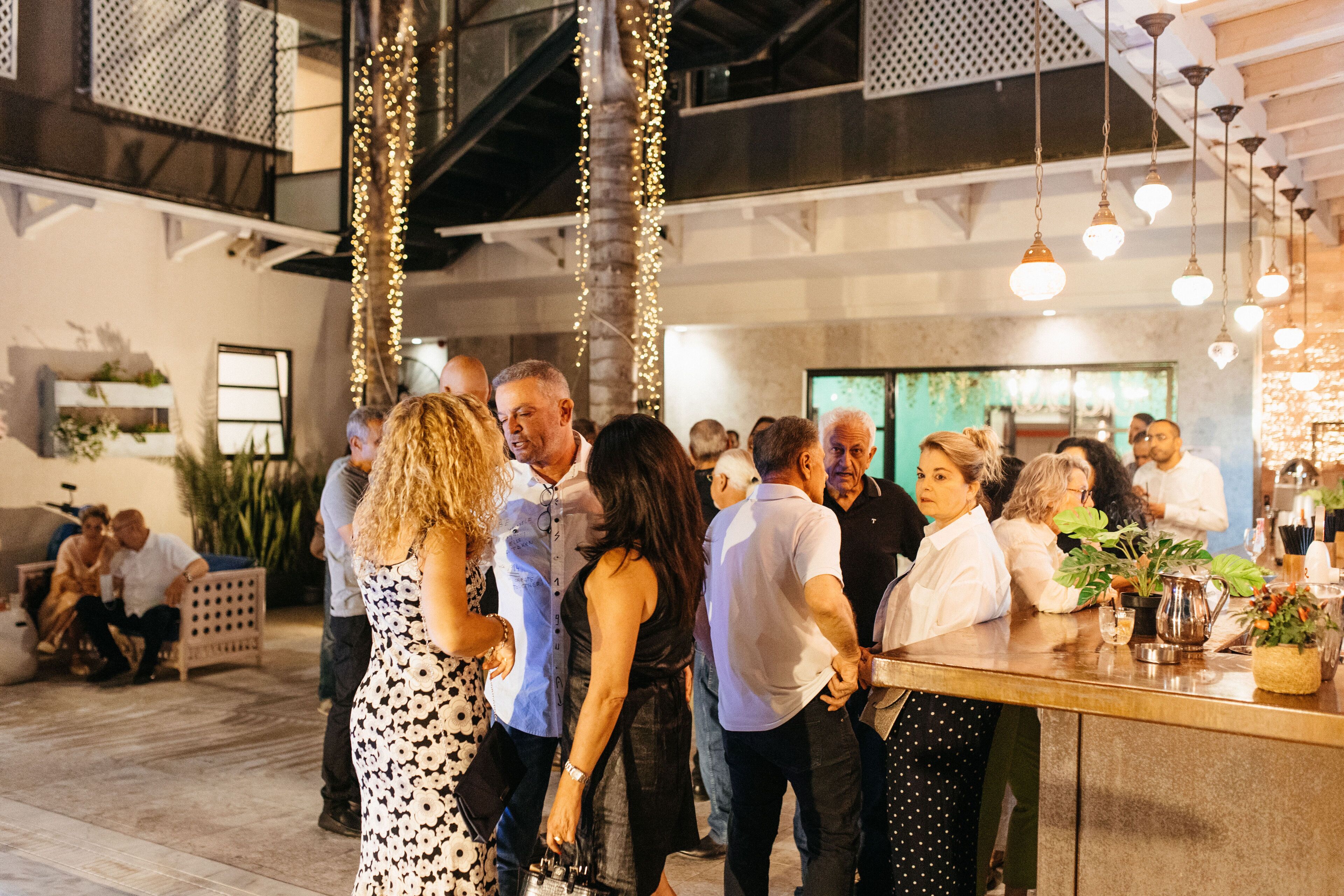A crowded indoor space with hanging lights, a bar area, and people interacting.