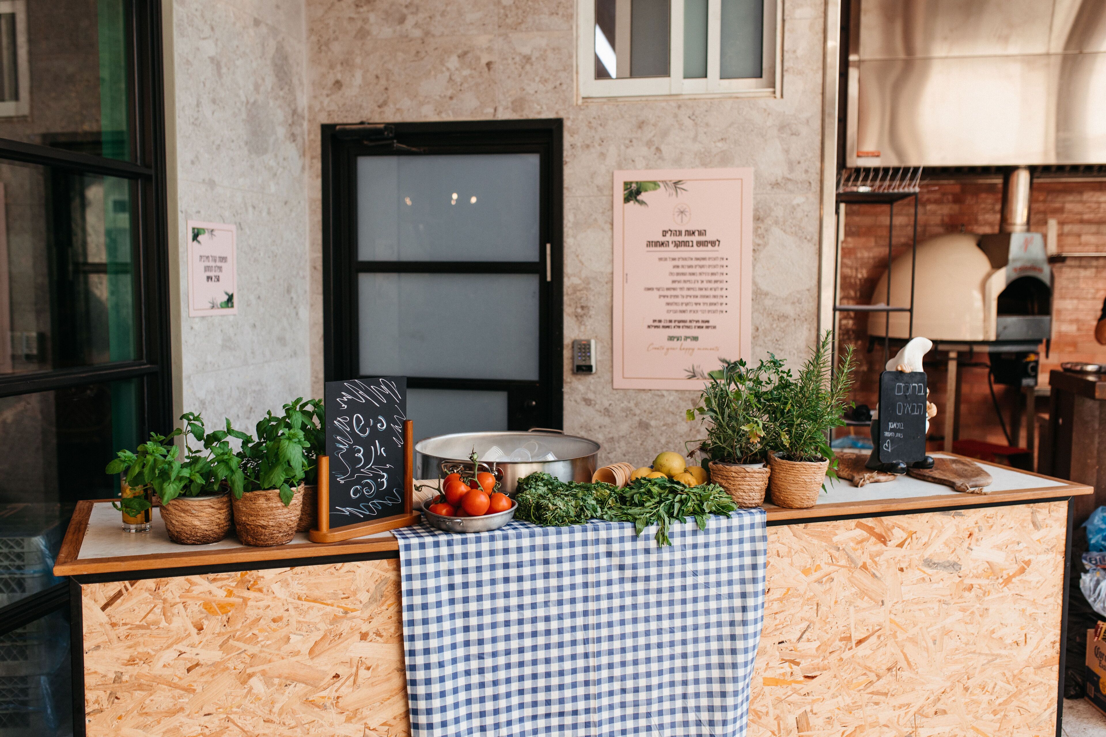 A kitchen counter with fresh produce, a chalkboard menu, and a brick oven.