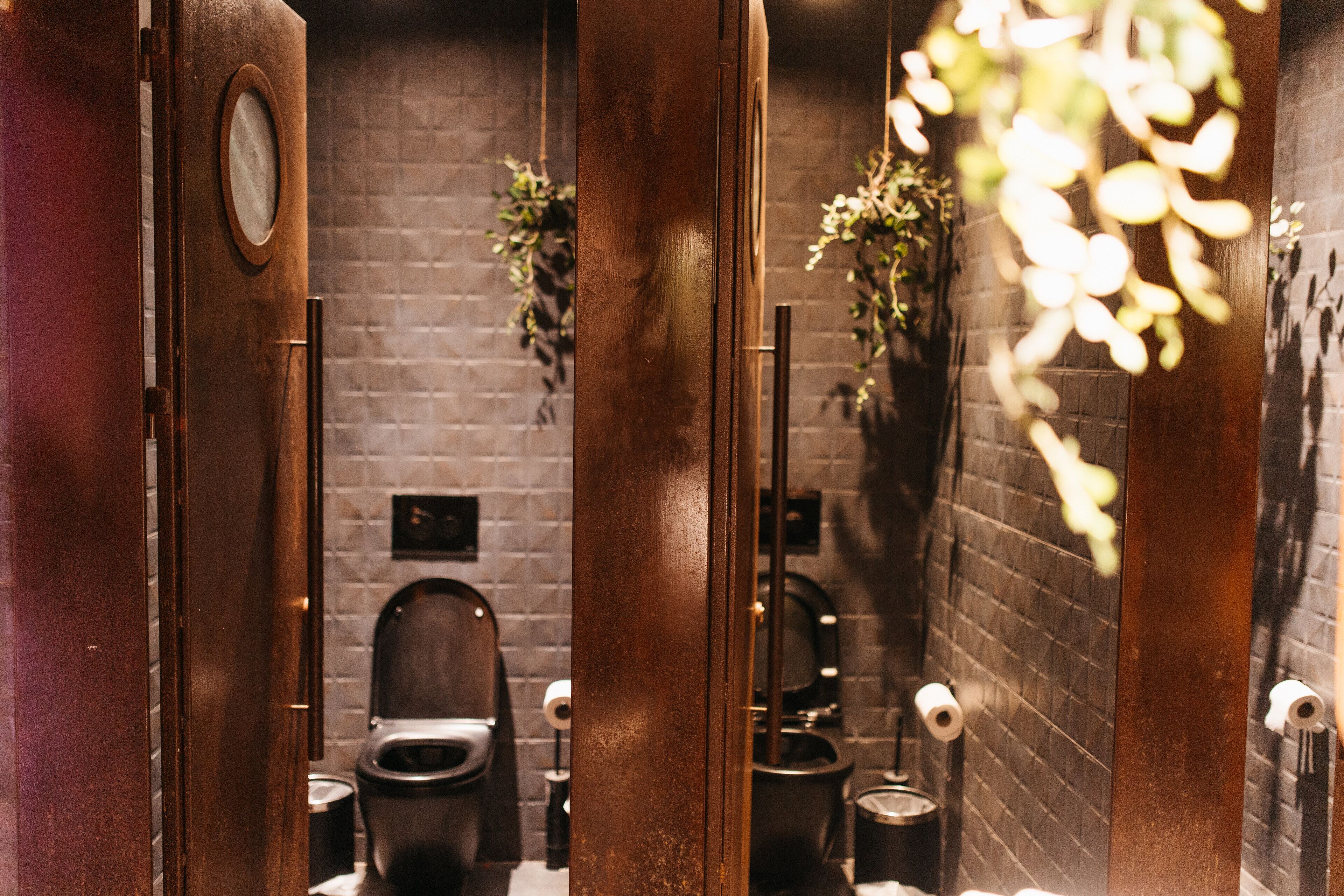A public restroom with two toilets, a wooden door, and a brick wall.