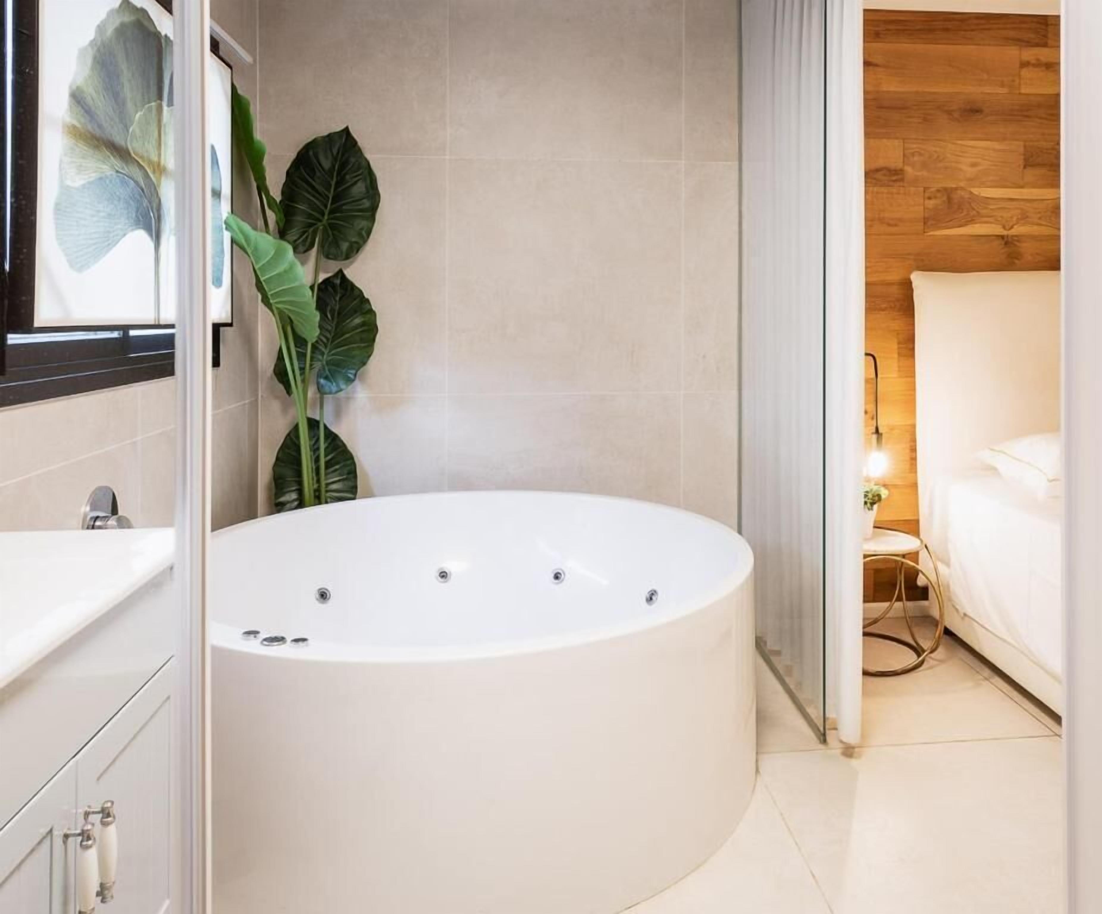 A modern bathroom with a freestanding bathtub, a large mirror, and a potted plant.