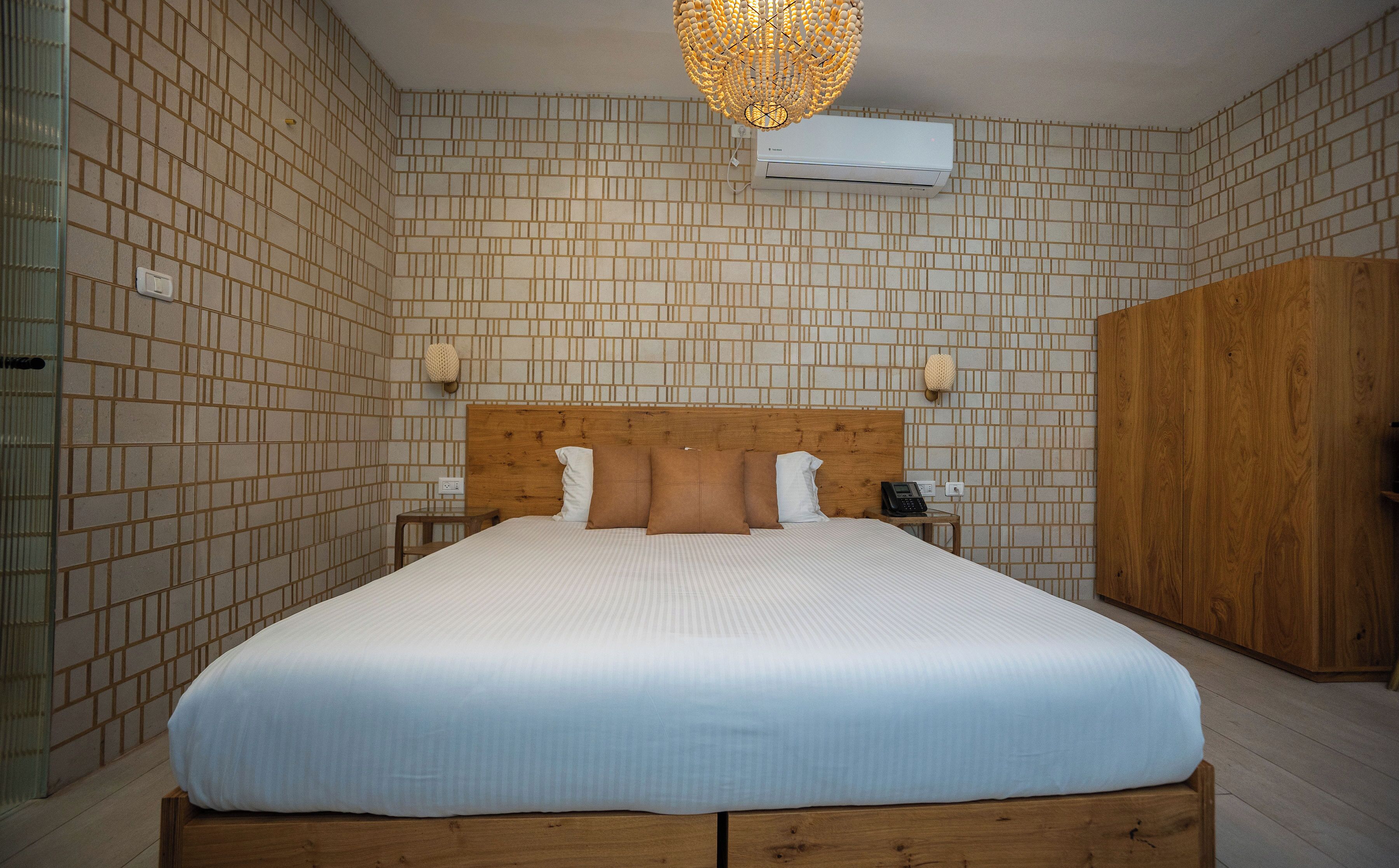 Een slaapkamer met een groot bed, een houten hoofdbord, nachtkastjes, een kledingkast en een wandairconditioner.