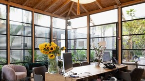 Un espace de bureau moderne doté d’un bureau en bois, de plusieurs chaises et de grandes fenêtres donnant sur un paysage verdoyant.