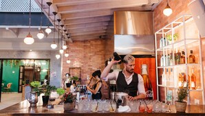 Un espace bar avec des luminaires suspendus, un barman préparant des boissons et des étagères remplies de bouteilles.