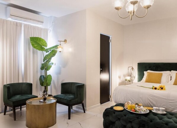 A modern hotel room with a large bed, two green armchairs, a round coffee table, and a potted plant. - Estate Spa (Rehovot)