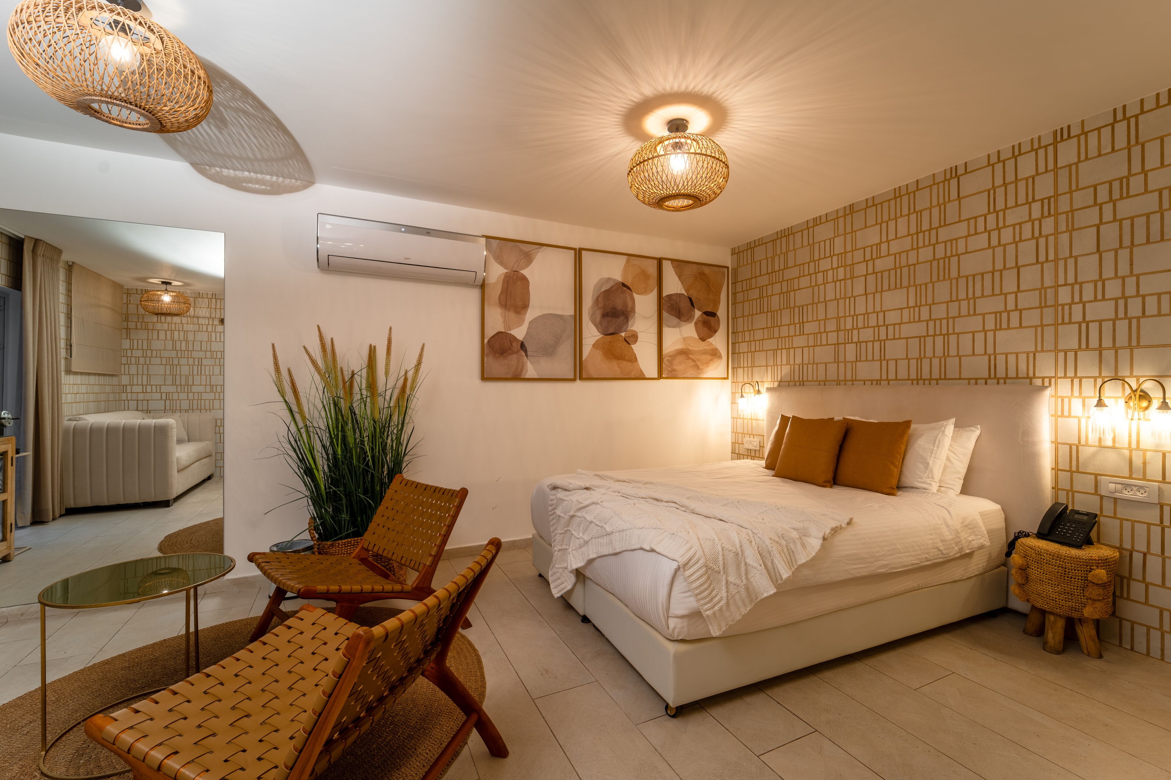 Um quarto moderno com uma cama grande, um espaço de estar com uma cadeira e uma mesa, e um detalhe decorativo na parede.