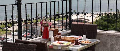 A balcony table with a meal, a vase of flowers, and a view of the sea.