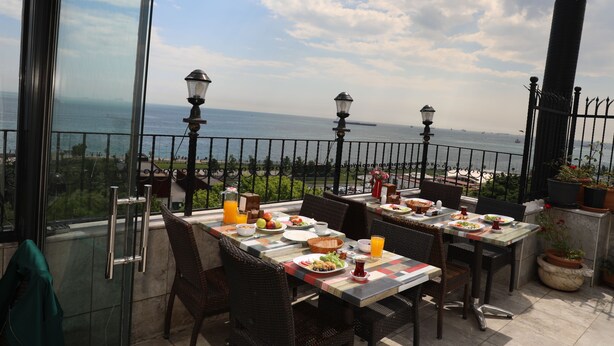 Un área de comedor al aire libre con mesas dispuestas para el desayuno, con vista a un cuerpo de agua y una costa distante.