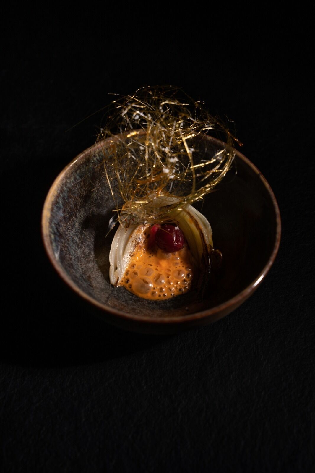 Un postre en un tazón oscuro con una cobertura dorada y elaborada.