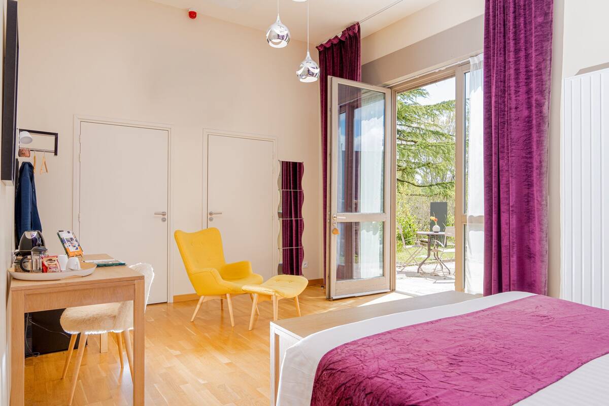 A modern bedroom with a bed, a desk, and a chair. There is a sliding glass door leading to an outdoor area.