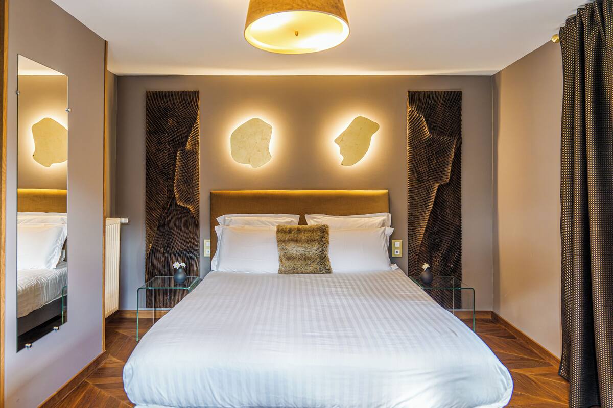 A modern hotel room with a large bed, a glass bedside table, and a unique wall design.