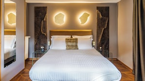 A modern hotel room with a large bed, a glass bedside table, and a unique wall design.
