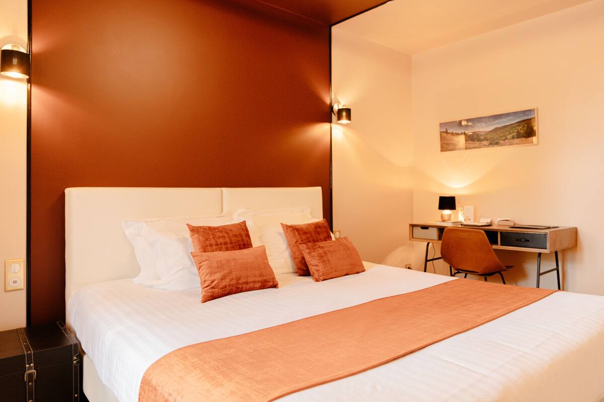 A hotel room with a large bed, a desk, and a chair.