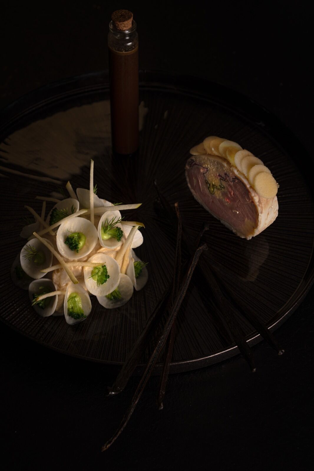 A plate with a meat dish and clams garnished with broccoli, a bottle, and a pair of chopsticks.