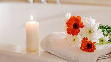 Un baño con una bañera blanca, una vela encendida y una toalla con flores.