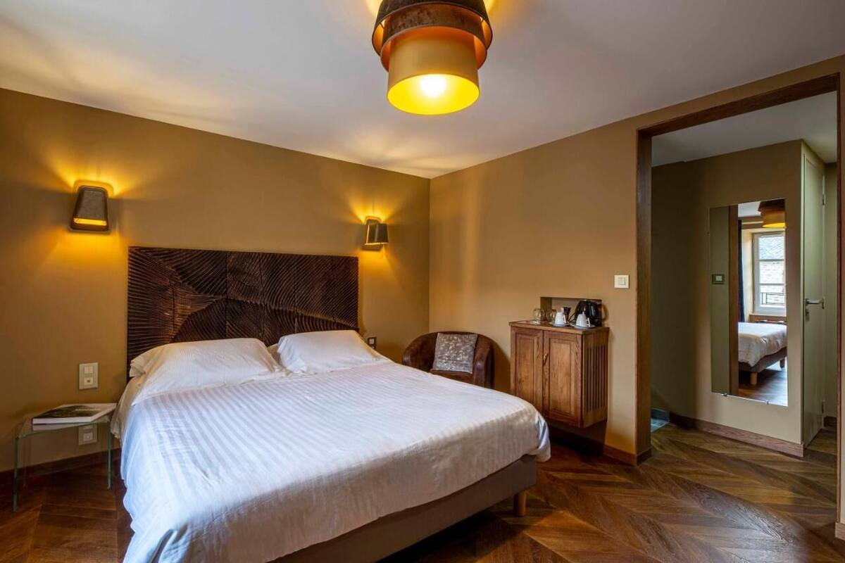 A hotel room with a large bed, two wall-mounted lamps, a wooden headboard, a small table with a book, and a cabinet.