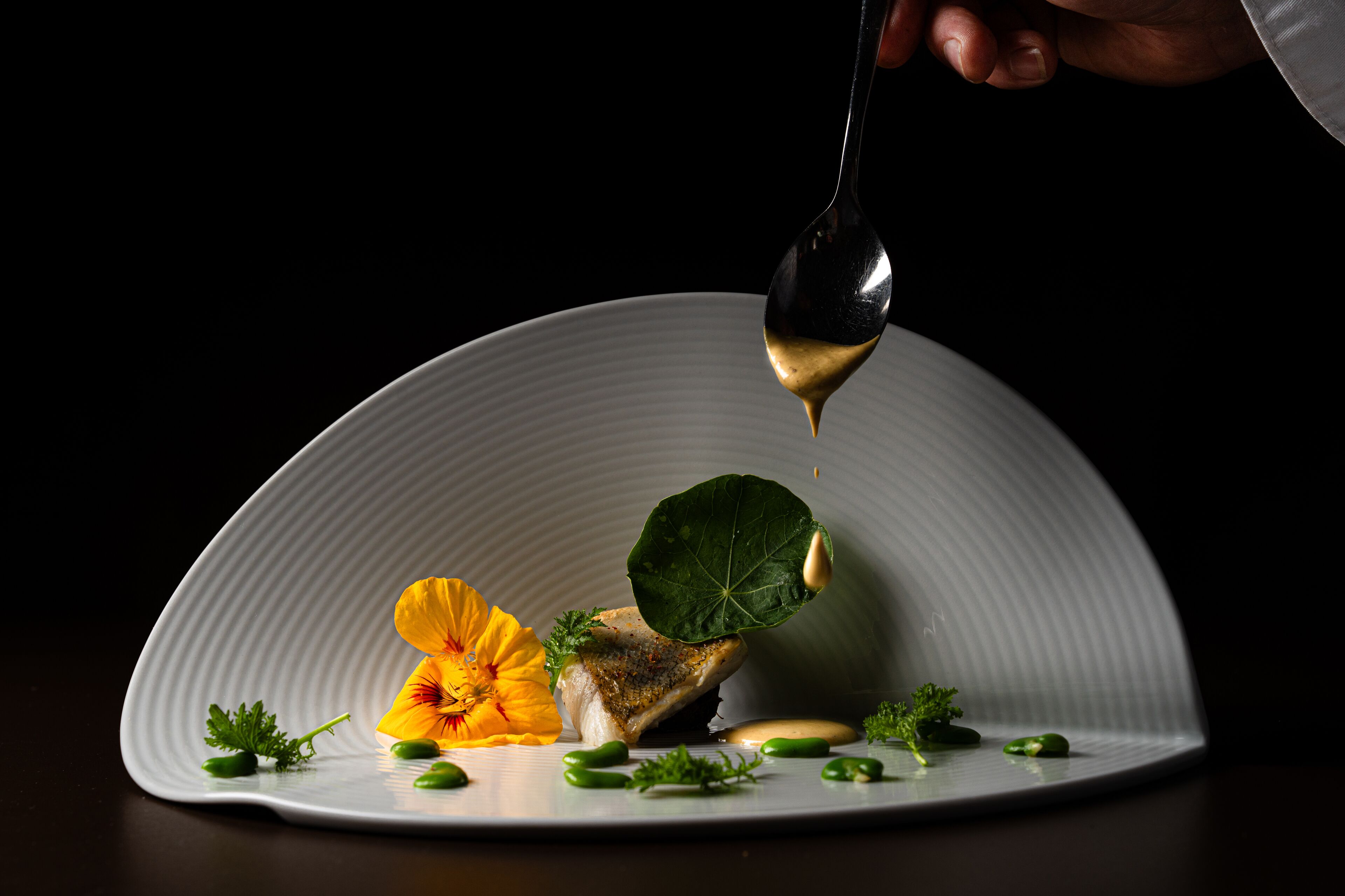 Un plato blanco con un pescado, guisantes verdes y una flor.