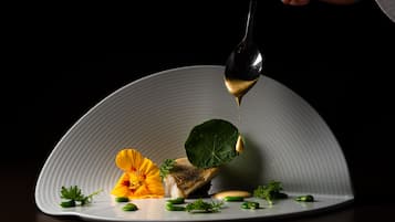 Un plato blanco con un pescado, guisantes verdes y una flor.