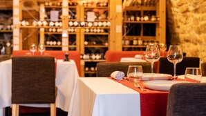 A restaurant with tables set for dining, a wine rack in the background, and a stone wall.