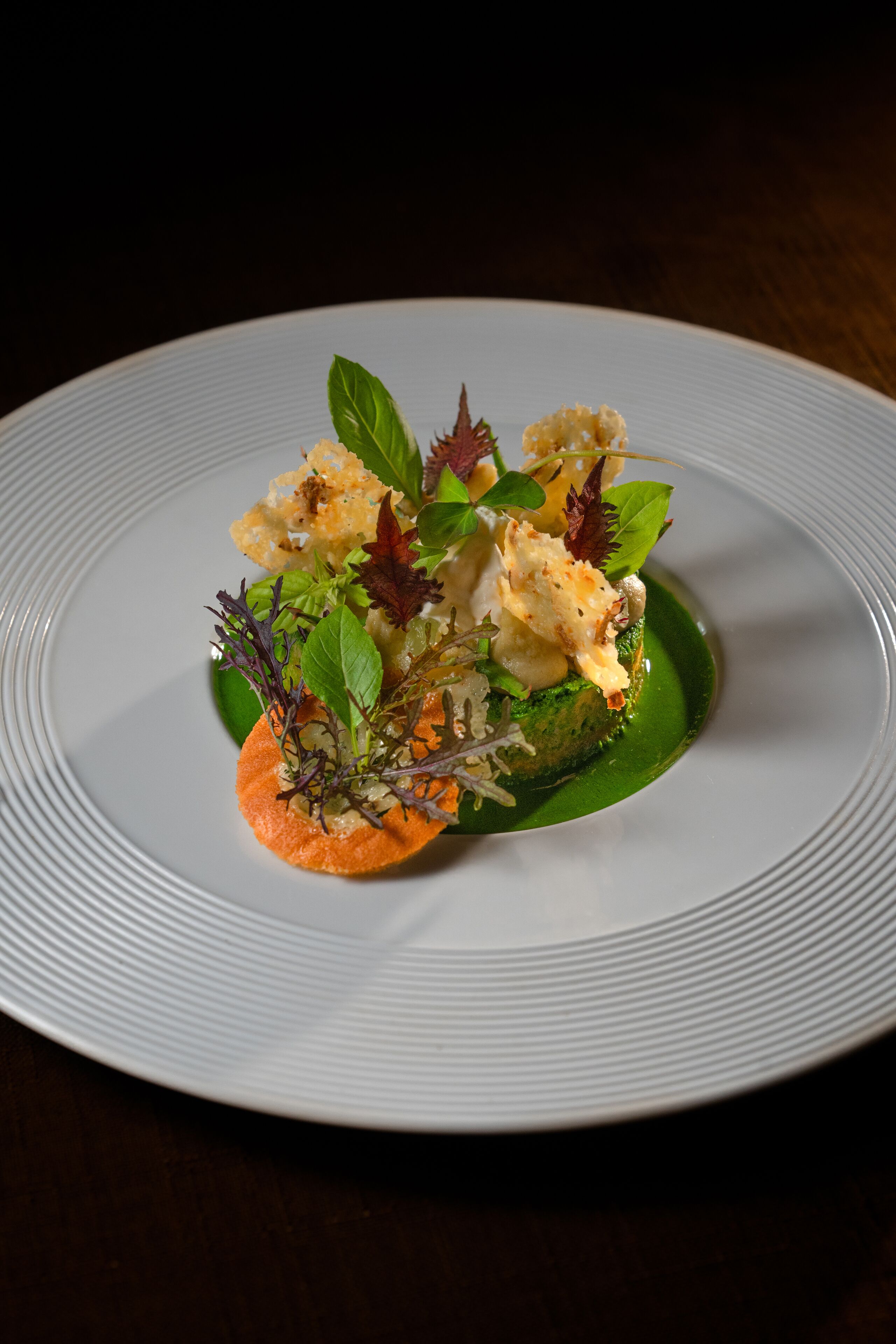Une assiette blanche avec une sauce verte et un plat principal décoré de feuilles et d’herbes.
