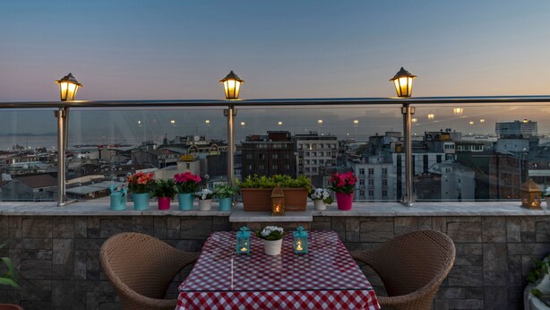 Una terraza con mesa y sillas, plantas en macetas y faroles.