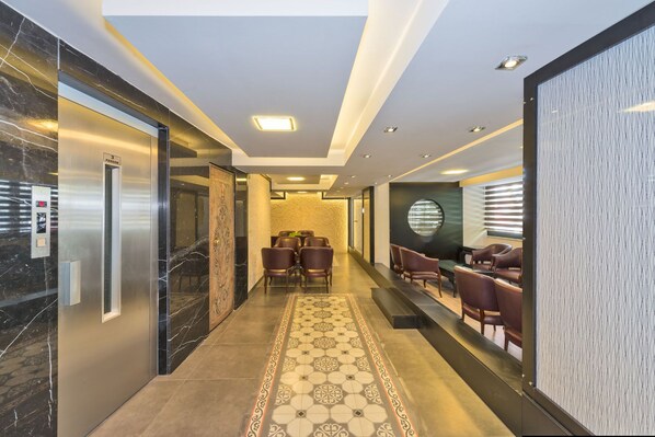 Un moderno vestíbulo de hotel con piso de mármol, un área de estar central con sillones de cuero y un mostrador de recepción.