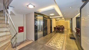 Un moderno vestíbulo de hotel con una escalera de mármol, una alfombra estampada y una zona de estar con sillones.