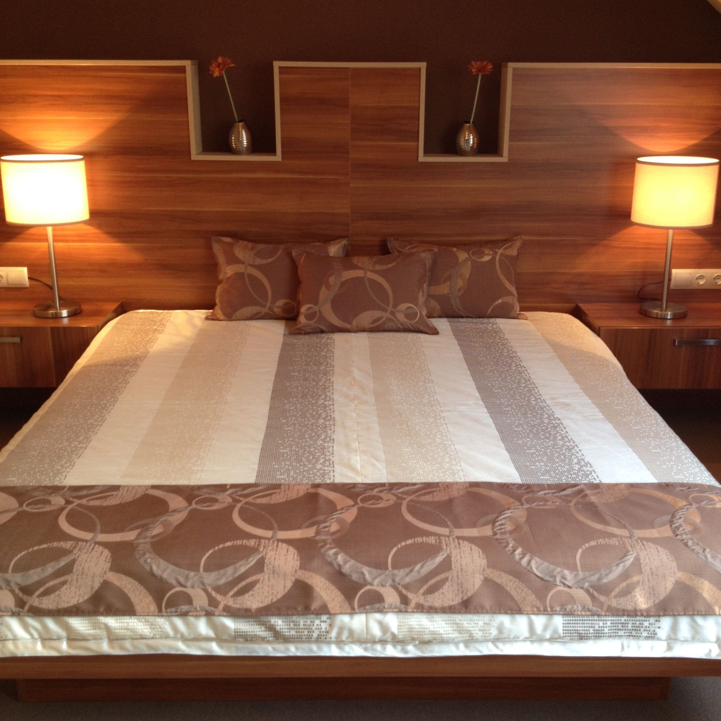 A hotel room with a large bed, two bedside lamps, and a wooden headboard with built-in shelves.