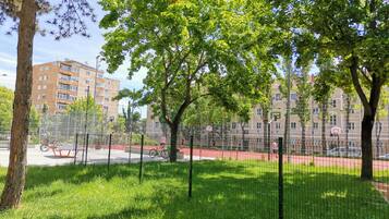 Una cancha de baloncesto rodeada de árboles y una valla, con edificios al fondo.