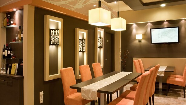 Un espace repas avec une longue table, des chaises orange et des luminaires suspendus.