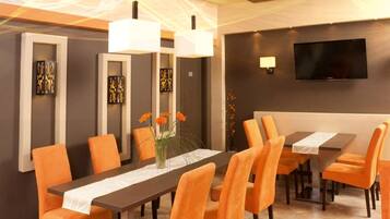 Un comedor moderno con una larga mesa, sillas naranjas e iluminación colgante.
