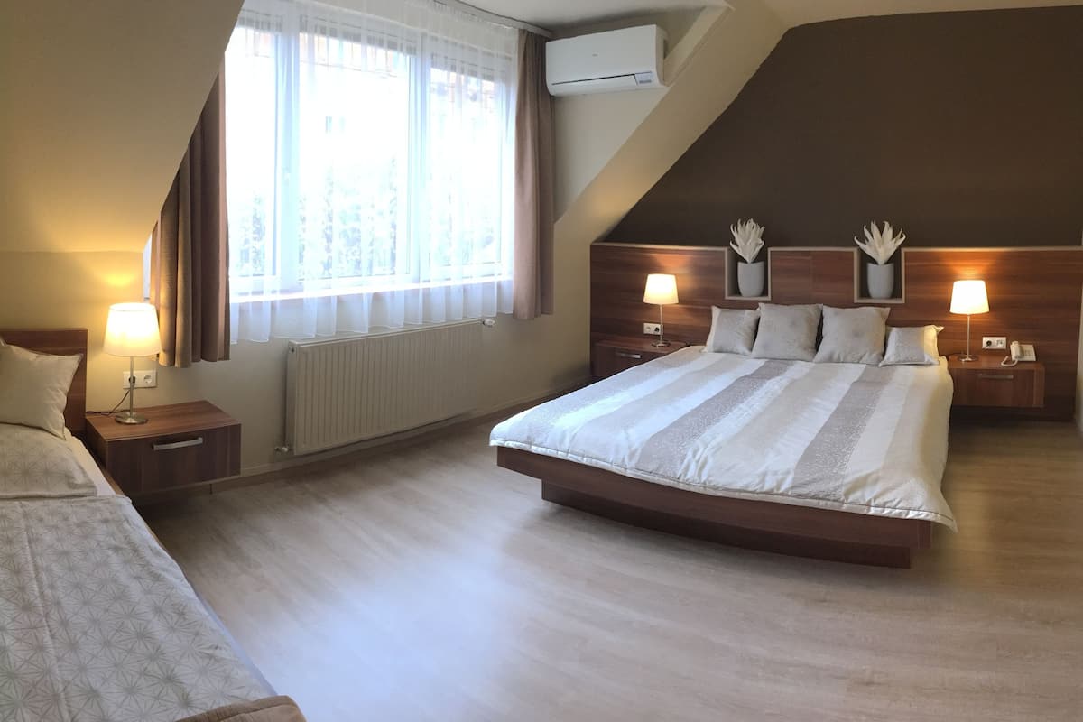 Une chambre d’hôtel avec un grand lit, un plus petit lit, deux tables de chevet avec des lampes, une fenêtre avec des rideaux et un radiateur.