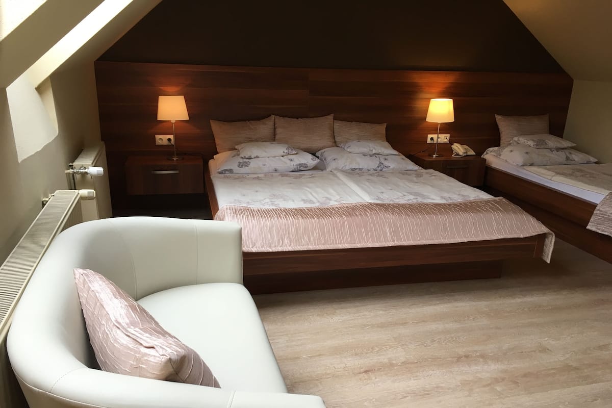 Une chambre avec un grand lit, deux tables de chevet avec des lampes, un fauteuil blanc et un plancher en bois.