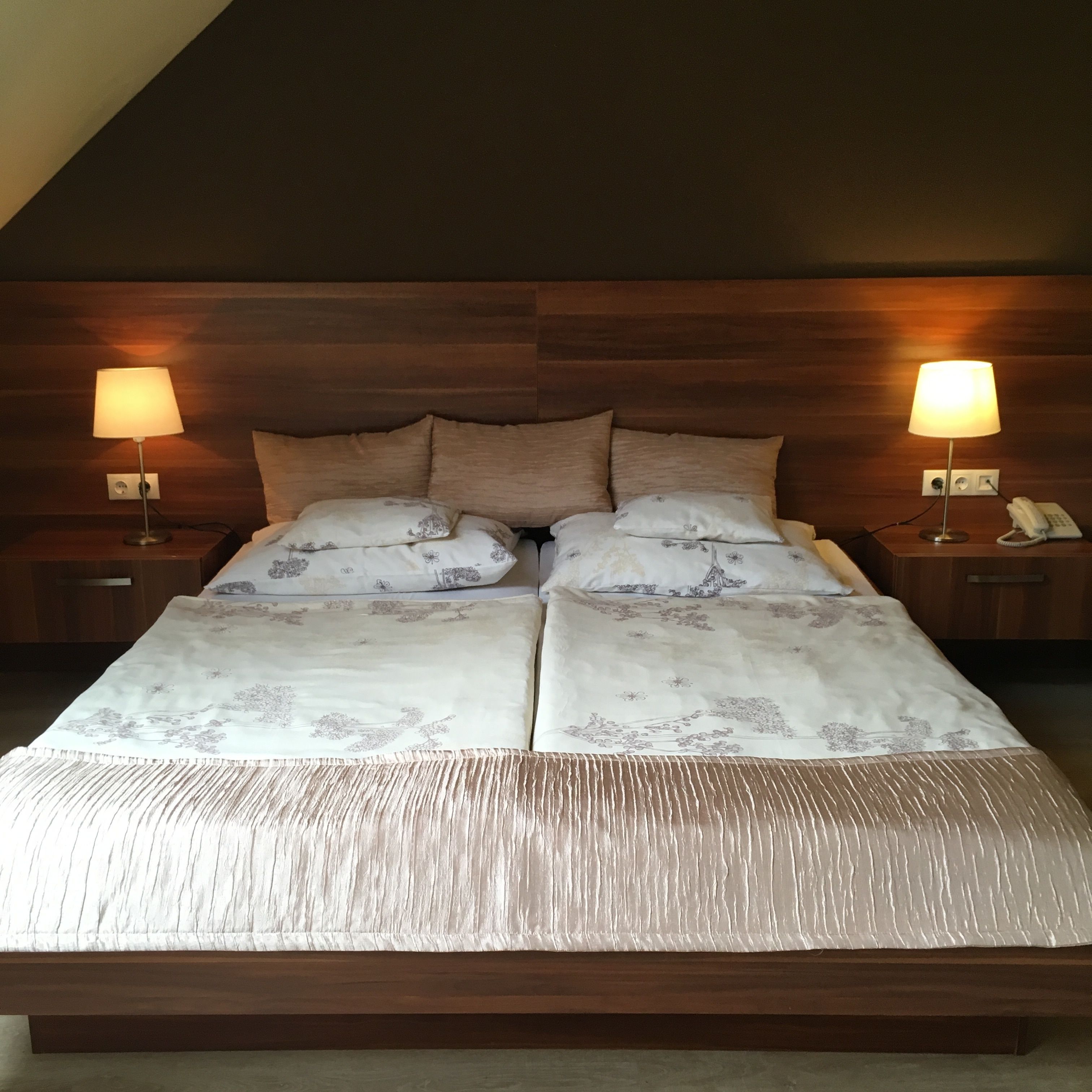 Ein Doppelbett mit Holz Kopfteil, zwei Nachttische mit Lampen und ein Telefon auf einem der Tische.
