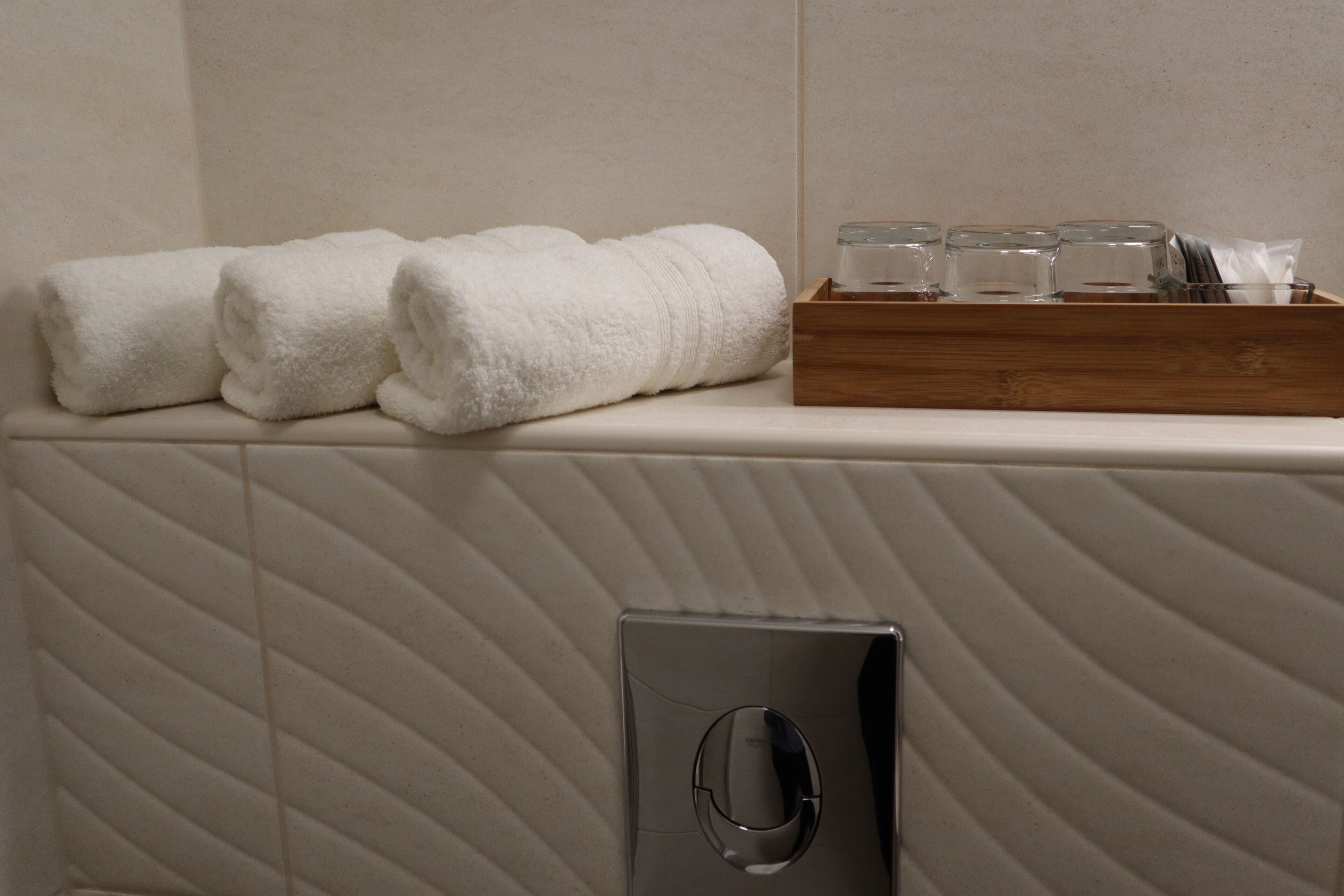 A bathroom with a towel rack holding three towels, a tray with glasses and a tissue, and a soap dispenser.