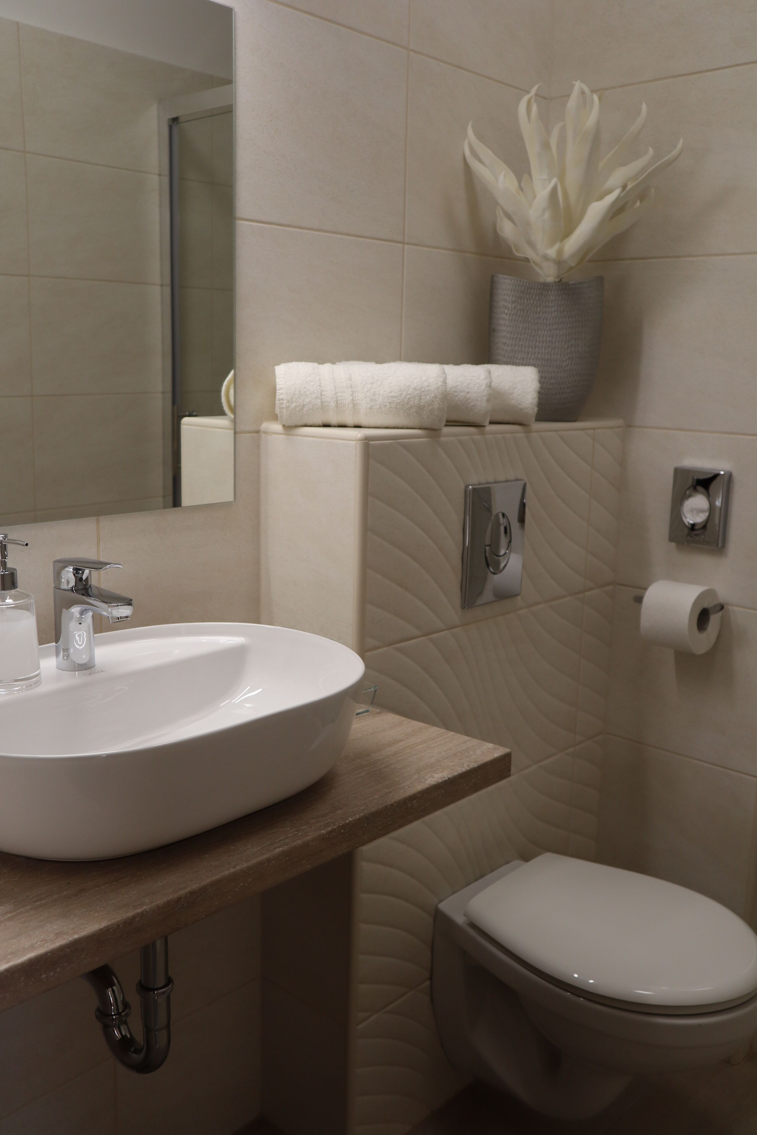Ein Badezimmer mit weißem Waschbecken, einem Spiegel, einer Toilette und einem an der Wand montierten Papierspender.
