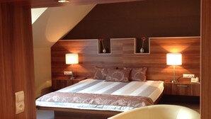 Une chambre d’hôtel moderne avec un plafond en bois, un grand lit recouvert d’une courtepointe à motifs, deux lampes de chevet et une chaise blanche.