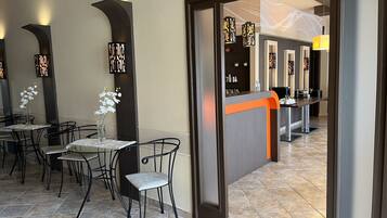 A hotel lobby with a reception desk, seating area with chairs and tables, and a decorative wall with arches.