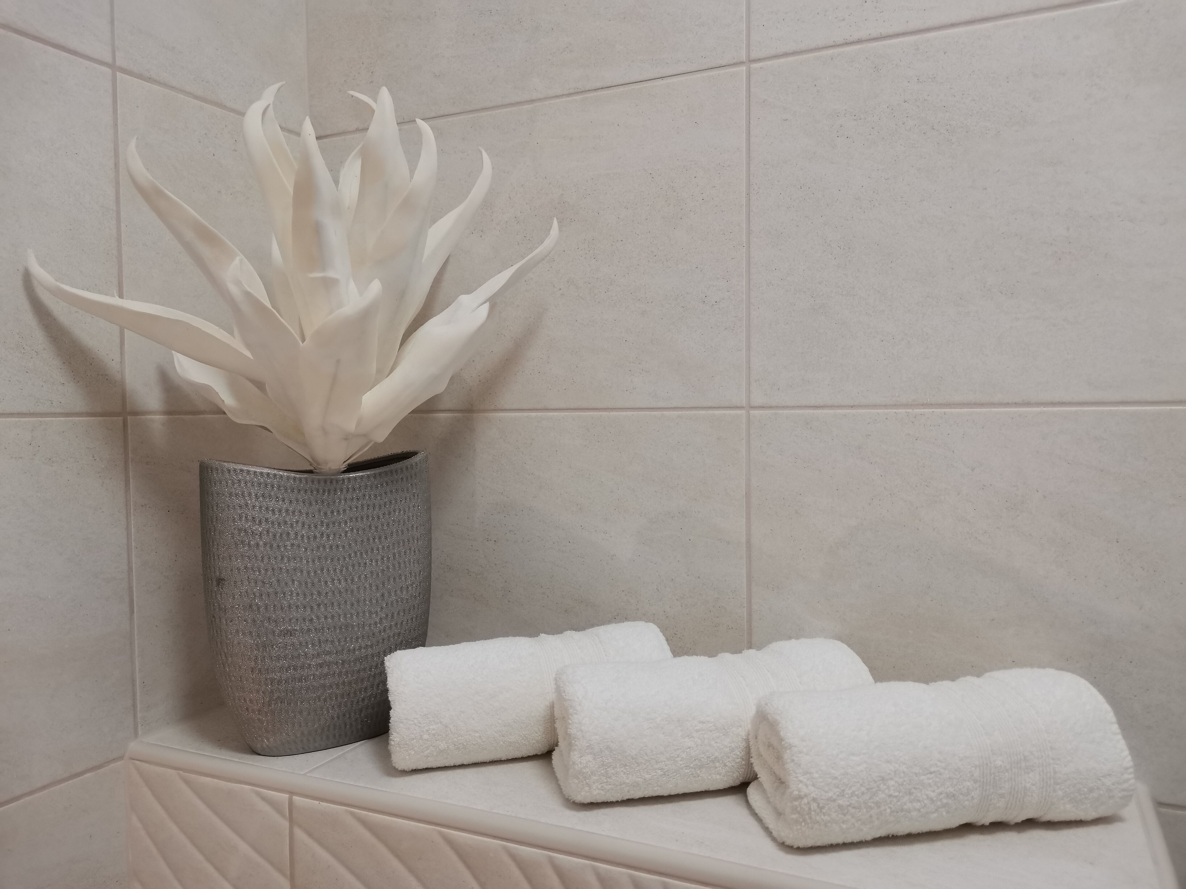Un baño con una planta blanca en un florero texturizado, una toalla y un muro con azulejos.